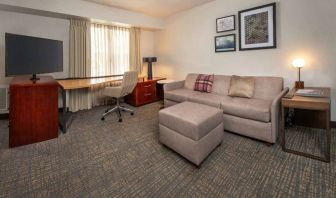 Sonesta ES Suites Baltimore BWI Airport guest room workspace, featuring chair, desk, and TV, plus a sofa nearby.