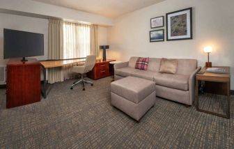 Sonesta ES Suites Baltimore BWI Airport guest room workspace, featuring chair, desk, and TV, plus a sofa nearby.