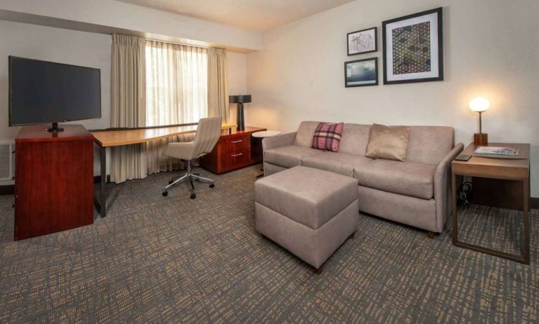 Sonesta ES Suites Baltimore BWI Airport guest room workspace, featuring chair, desk, and TV, plus a sofa nearby.