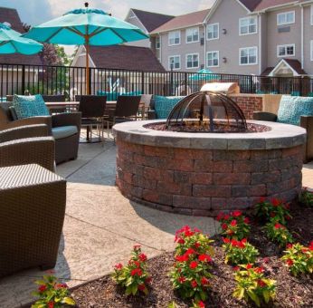 Sonesta ES Suites Allentown Bethlehem Airport’s fire pit has armchairs arranged around it, with the pool and a flowerbed nearby.