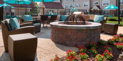 Sonesta ES Suites Allentown Bethlehem Airport’s fire pit has armchairs arranged around it, with the pool and a flowerbed nearby.