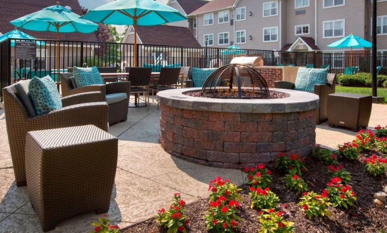 Sonesta ES Suites Allentown Bethlehem Airport’s fire pit has armchairs arranged around it, with the pool and a flowerbed nearby.