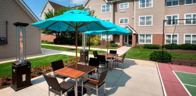 Sonesta ES Suites Allentown Bethlehem Airport’s patio is furnished with shaded tables and chairs.