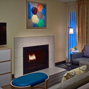 Sonesta ES Suites Cincinnati - Blue Ash guest room lounge, furnished with sofa, armchair, TV, and fireplace.