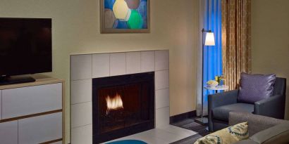 Sonesta ES Suites Cincinnati - Blue Ash guest room lounge, furnished with sofa, armchair, TV, and fireplace.