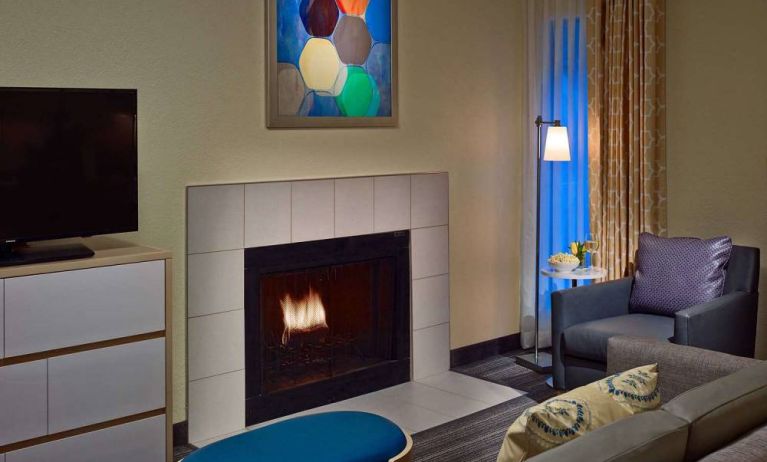 Sonesta ES Suites Cincinnati - Blue Ash guest room lounge, furnished with sofa, armchair, TV, and fireplace.