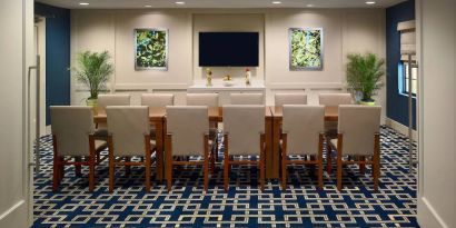 Hotel meeting room, decorated with potted plants and wall art, and featuring a dozen chairs around a long table.