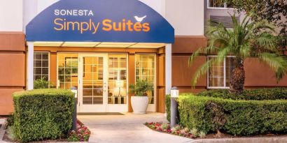 Sonesta Simply Suites Irvine East Foothill’s exterior features a covered entranceway, clear signage, and pleasant greenery.