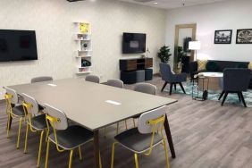 Sonesta Miami Airport meeting room facility, with long table, wall-mounted TV, and nearby armchair and sofa seating. 