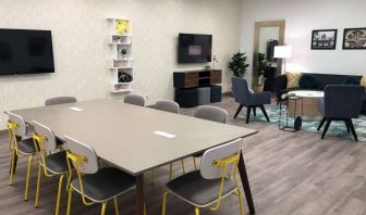 Sonesta Miami Airport meeting room facility, with long table, wall-mounted TV, and nearby armchair and sofa seating. 