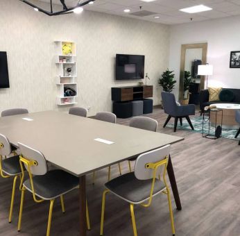 Sonesta Miami Airport meeting room facility, with long table, wall-mounted TV, and nearby armchair and sofa seating. 