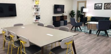 Sonesta Miami Airport meeting room facility, with long table, wall-mounted TV, and nearby armchair and sofa seating. 