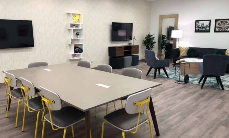 Sonesta Miami Airport meeting room facility, with long table, wall-mounted TV, and nearby armchair and sofa seating. 