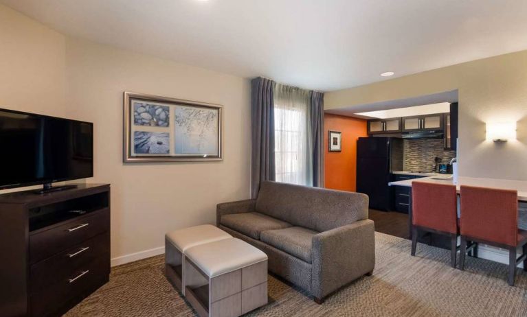 Guest room in Sonesta ES Suites Dulles Airport, featuring sofa and widescreen TV, with nearby kitchenette.