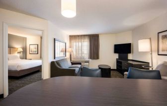 Sonesta Simply Suites Baltimore BWI Airport double bed guest room, featuring living area with sofa, TV, and window.