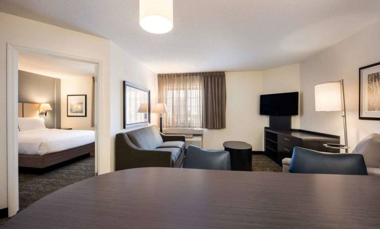 Sonesta Simply Suites Baltimore BWI Airport double bed guest room, featuring living area with sofa, TV, and window.