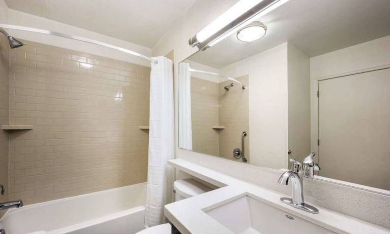 Guest bathroom furnished with sink and wide mirror, plus shower and bathtub.