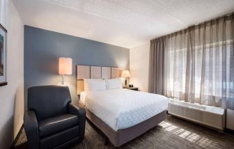 Double bed guest room in Sonesta Simply Suites Cleveland North Olmsted Airport, including armchair and windows.