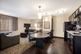 Sonesta Simply Suites Nashville Brentwood guest room workspace, featuring desk and multiple chairs, with TV and kitchenette close at hand.