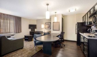 Sonesta Simply Suites Nashville Brentwood guest room workspace, featuring desk and multiple chairs, with TV and kitchenette close at hand.