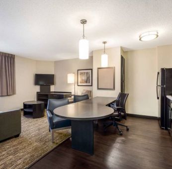 Sonesta Simply Suites Nashville Brentwood guest room workspace, featuring desk and multiple chairs, with TV and kitchenette close at hand.