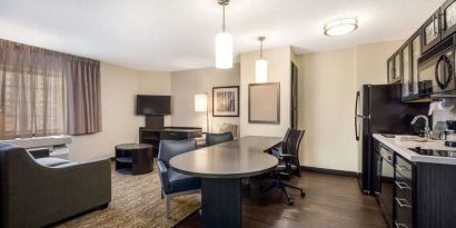 Sonesta Simply Suites Nashville Brentwood guest room workspace, featuring desk and multiple chairs, with TV and kitchenette close at hand.