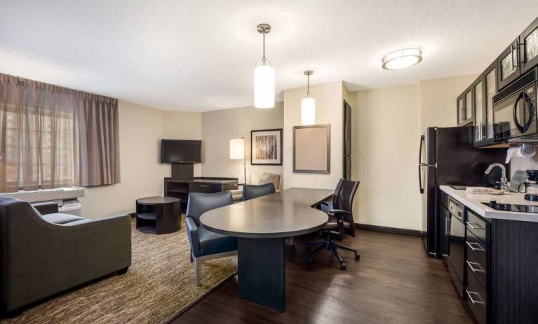 Sonesta Simply Suites Nashville Brentwood guest room workspace, featuring desk and multiple chairs, with TV and kitchenette close at hand.