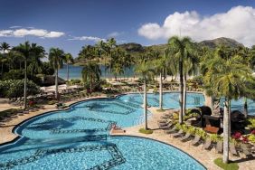 The hotel’s outdoor pool includes sun loungers and tall trees nearby.