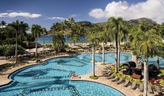 The hotel’s outdoor pool includes sun loungers and tall trees nearby.