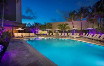 Sonesta Fort Lauderdale Beach’s outdoor pool has palm trees and sun loungers by the side, with shade available.