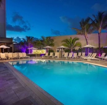 Sonesta Fort Lauderdale Beach’s outdoor pool has palm trees and sun loungers by the side, with shade available.