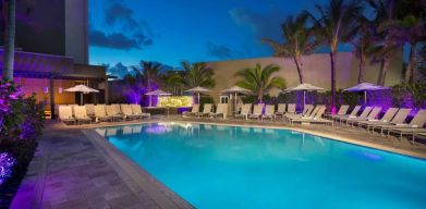 Sonesta Fort Lauderdale Beach’s outdoor pool has palm trees and sun loungers by the side, with shade available.