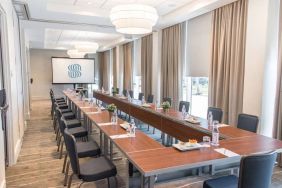 Sonesta Fort Lauderdale Beach meeting room, with a head table for one person and two long tables each with space for 10 attendees, and a projector screen.