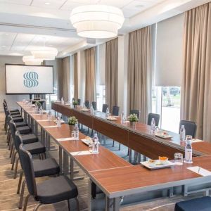 Sonesta Fort Lauderdale Beach meeting room, with a head table for one person and two long tables each with space for 10 attendees, and a projector screen.