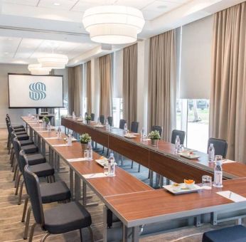 Sonesta Fort Lauderdale Beach meeting room, with a head table for one person and two long tables each with space for 10 attendees, and a projector screen.