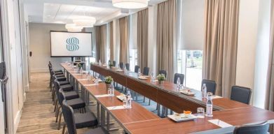 Sonesta Fort Lauderdale Beach meeting room, with a head table for one person and two long tables each with space for 10 attendees, and a projector screen.