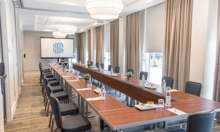 Sonesta Fort Lauderdale Beach meeting room, with a head table for one person and two long tables each with space for 10 attendees, and a projector screen.