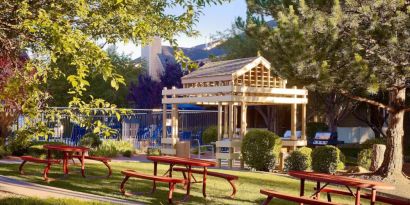 The picnic area at Sonesta ES Suites Flagstaff features benches on tables on grass, with trees and and barbecue facilities nearby.