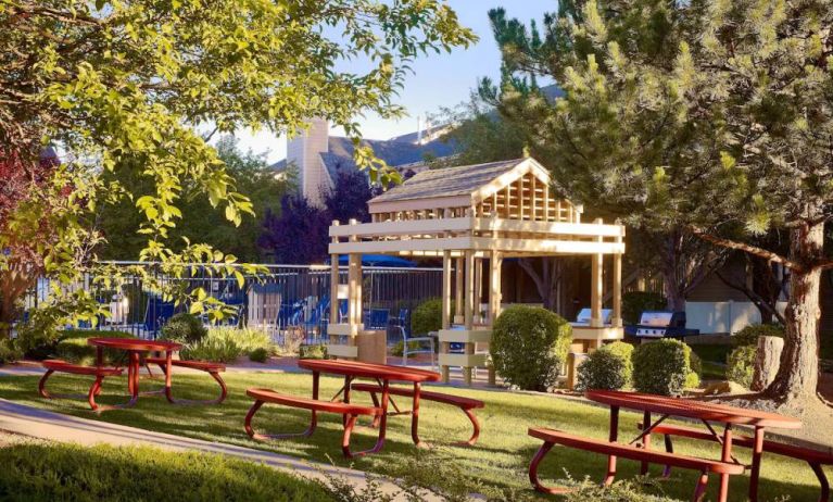 The picnic area at Sonesta ES Suites Flagstaff features benches on tables on grass, with trees and and barbecue facilities nearby.