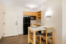 Sonesta ES Suites Charlotte Arrowood guest room kitchen area, with fridge-freezer, small table, sink, oven, and microwave.