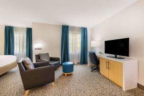 Sonesta ES Suites Charlotte Arrowood guest room workspace desk and chair, with nearby armchairs and television.