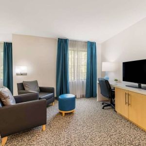 Sonesta ES Suites Charlotte Arrowood guest room workspace desk and chair, with nearby armchairs and television.