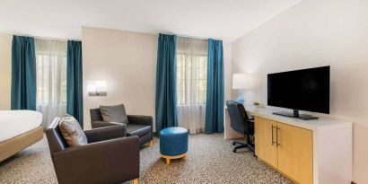 Sonesta ES Suites Charlotte Arrowood guest room workspace desk and chair, with nearby armchairs and television.