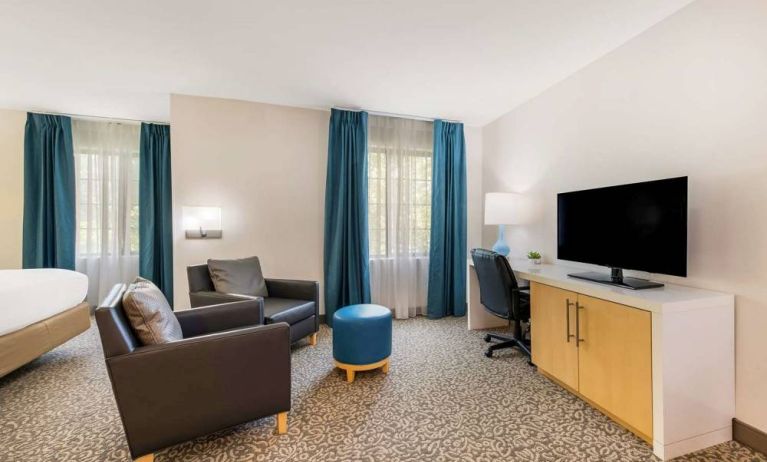 Sonesta ES Suites Charlotte Arrowood guest room workspace desk and chair, with nearby armchairs and television.