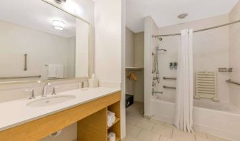 Guest bathroom in Sonesta ES Suites Charlotte Arrowood, furnished with large mirror, sink, bath and shower.