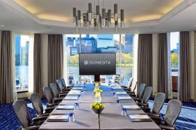 Royal Sonesta Boston meeting room, featuring large windows and high ceiling, long table and twelve surrounding chairs, plus widescreen TV.