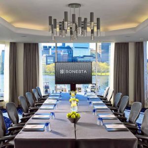 Royal Sonesta Boston meeting room, featuring large windows and high ceiling, long table and twelve surrounding chairs, plus widescreen TV.