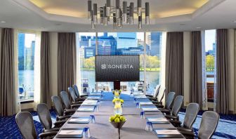 Royal Sonesta Boston meeting room, featuring large windows and high ceiling, long table and twelve surrounding chairs, plus widescreen TV.