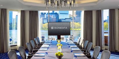 Royal Sonesta Boston meeting room, featuring large windows and high ceiling, long table and twelve surrounding chairs, plus widescreen TV.