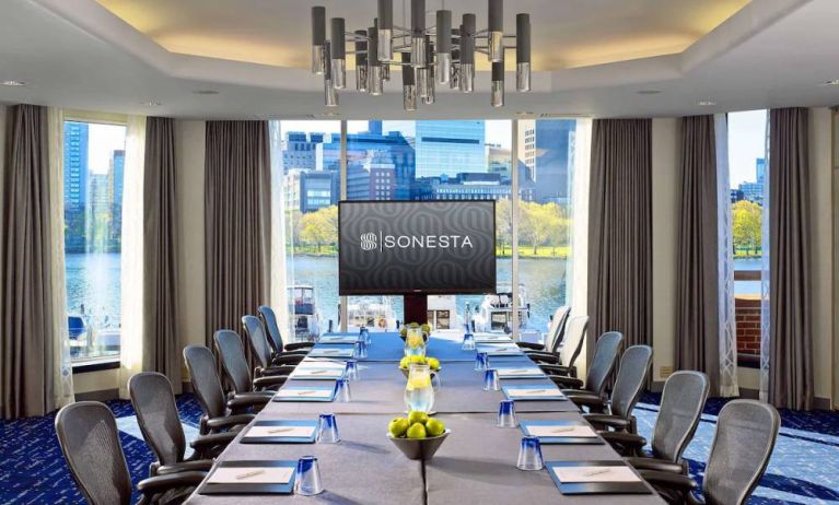 Royal Sonesta Boston meeting room, featuring large windows and high ceiling, long table and twelve surrounding chairs, plus widescreen TV.